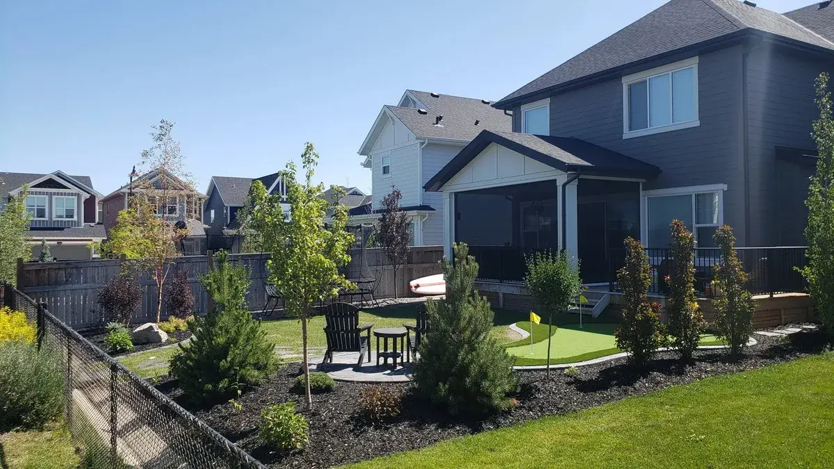 Backyard with lawn, young trees, shrubs and a patio beside a dark grey house