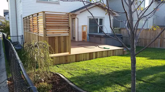 Low deck with a wood privacy screen next to a lawn and a small tree