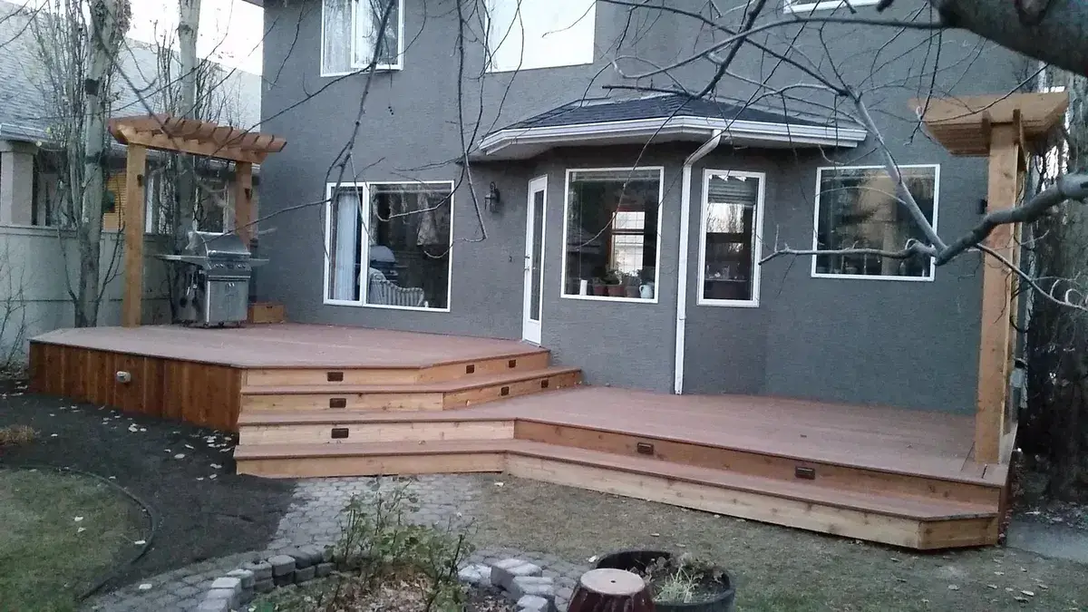 Wide two-level deck with steps and pergola posts behind a grey house
