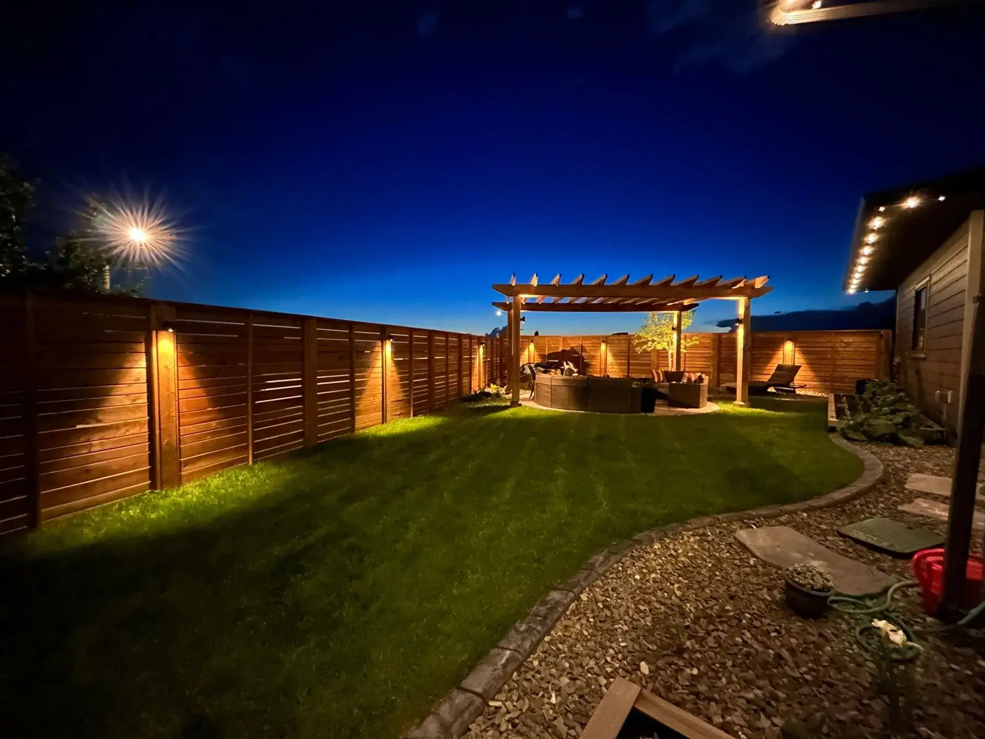 Backyard at dusk with a lit pergola, cedar fence and lawn