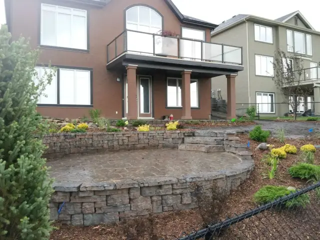 Curved stone retaining wall and planting beds below a large house