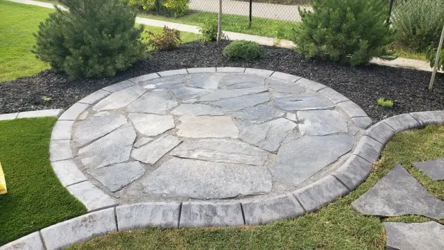 Round flagstone patio set into a lawn with planting beds